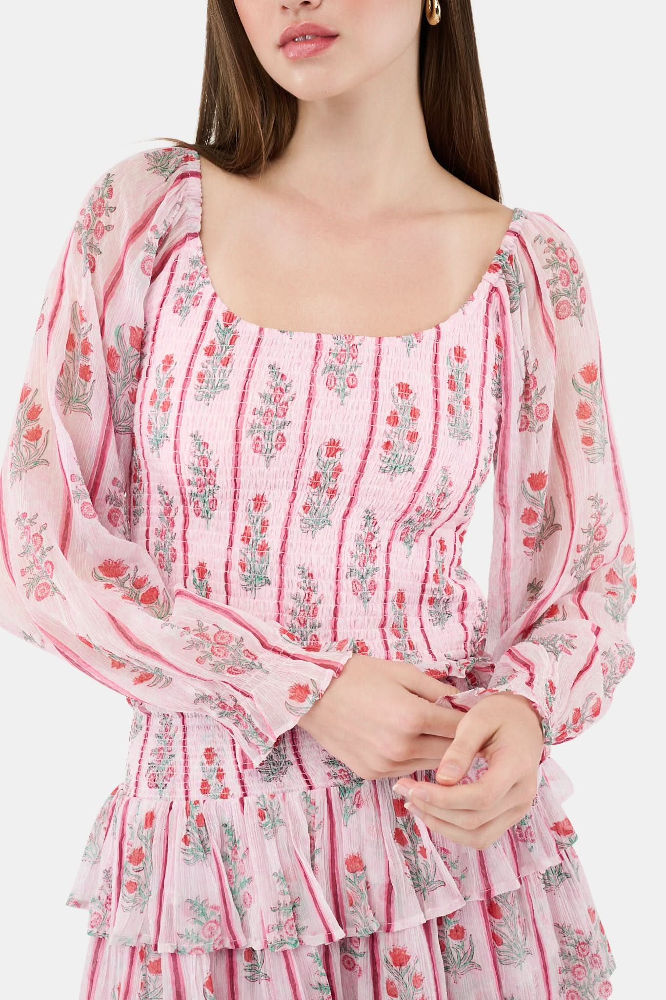 A woman with long brown hair models the Roller Rabbit Rose Ribbon Morgana Top—a pink, floral long-sleeve blouse—against a plain light background.