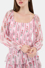 A woman with long brown hair models the Roller Rabbit Rose Ribbon Morgana Top—a pink, floral long-sleeve blouse—against a plain light background.