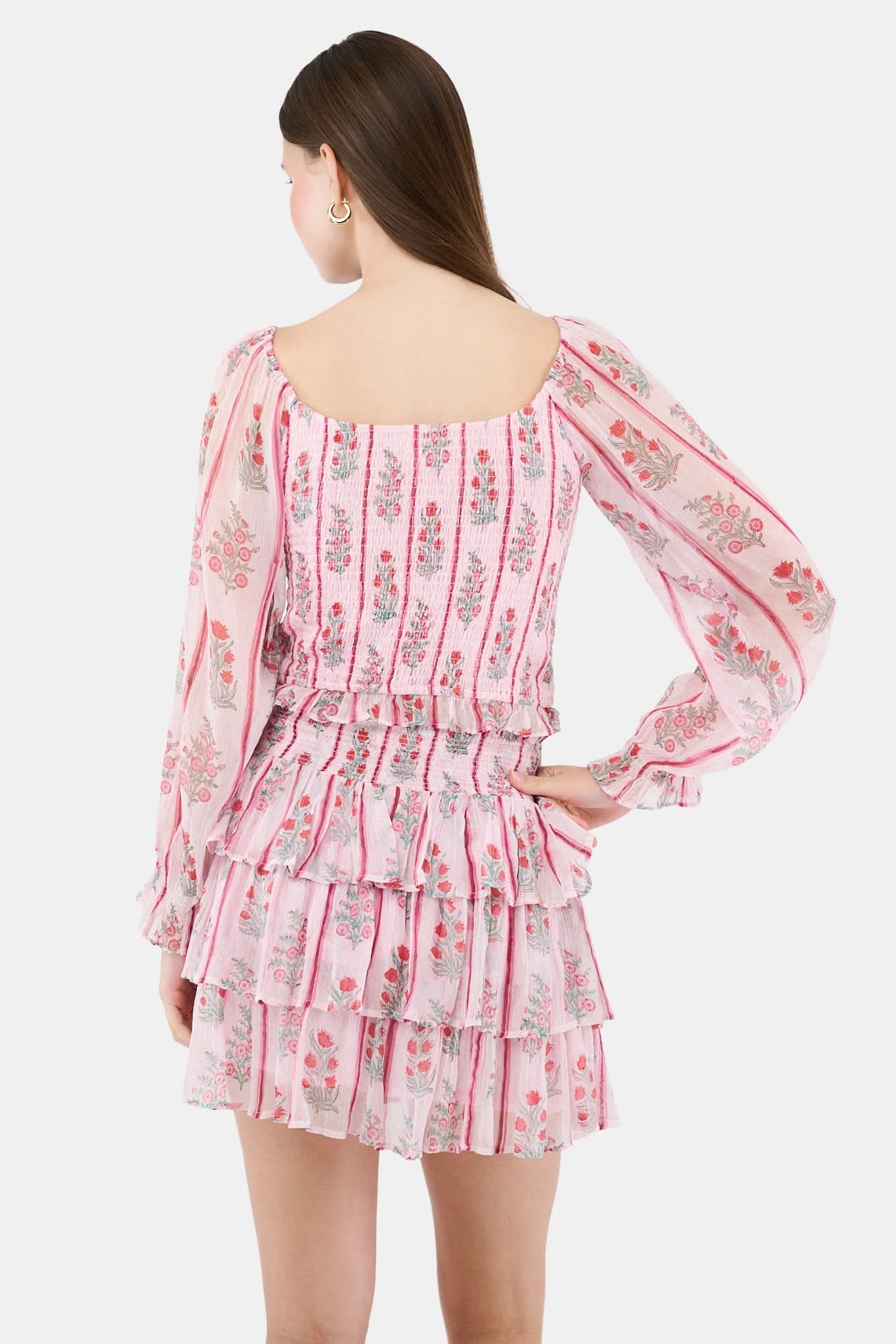 A woman with long brown hair models the Roller Rabbit Rose Ribbon Morgana Top—a pink, floral long-sleeve blouse—against a plain light background.
