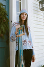 A young woman with fair skin and light makeup gazes at the camera, one hand on her hat, wearing a light blue Roller Rabbit Jemina Fairisle Beanie with a red and white pattern that matches her sweater.