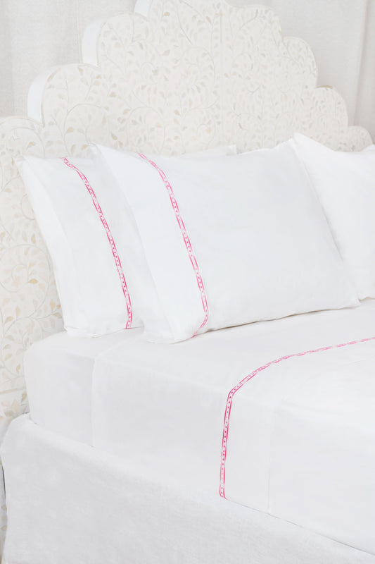 Two white Francis Embroidered Pillowcases by Roller Rabbit, made of 100 cotton with a 300 thread count, are arranged on a matching bed. A scalloped, floral headboard provides an elegant backdrop.