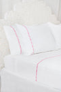 Two white Francis Embroidered Pillowcases by Roller Rabbit, made of 100 cotton with a 300 thread count, are arranged on a matching bed. A scalloped, floral headboard provides an elegant backdrop.