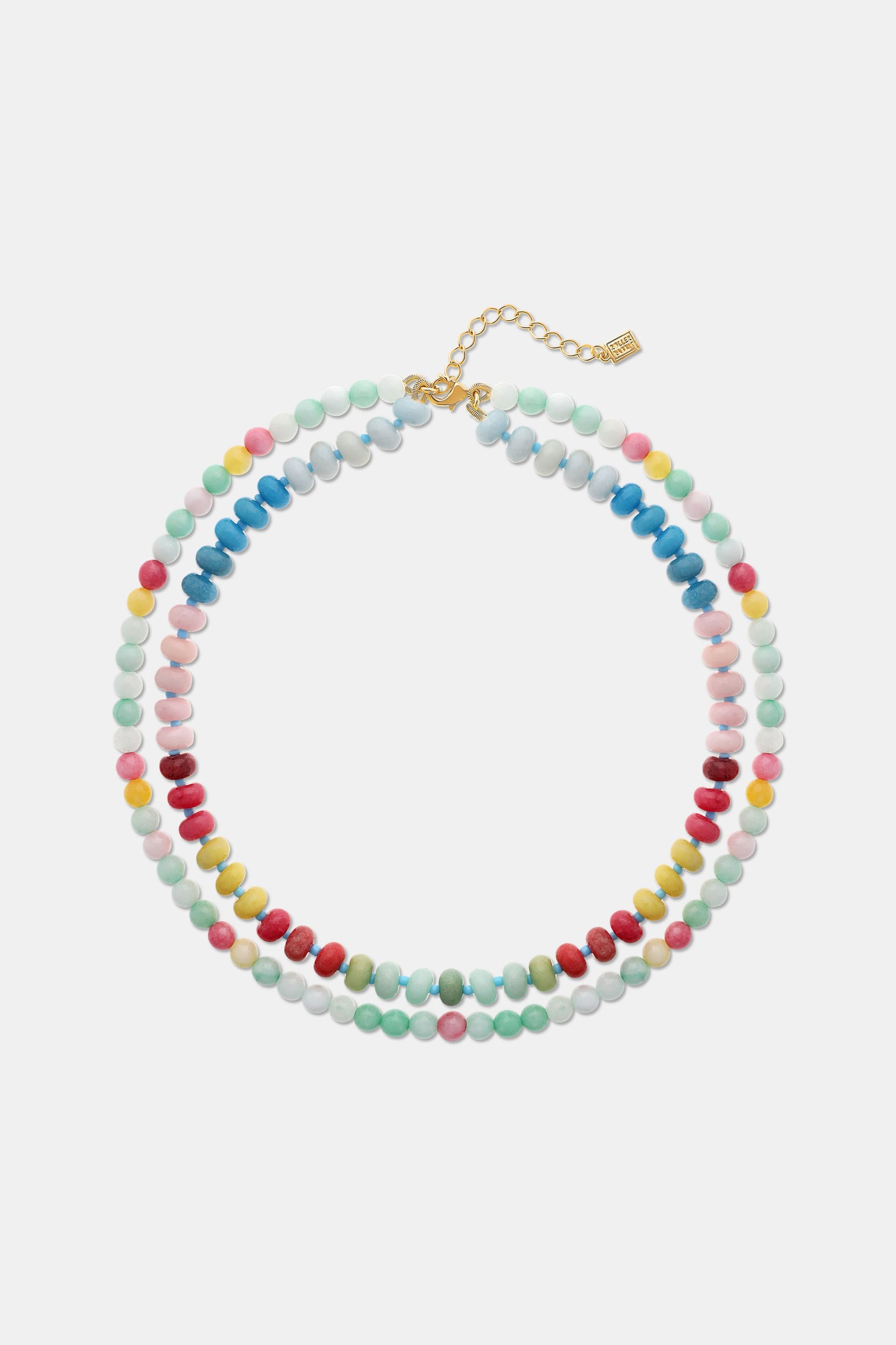 A woman is shown from the shoulders up wearing a cream knit top and the Roller Rabbit Beaded Necklace Stack, featuring colorful beaded chains and a small white flower-shaped bead.