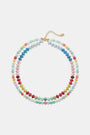 A woman is shown from the shoulders up wearing a cream knit top and the Roller Rabbit Beaded Necklace Stack, featuring colorful beaded chains and a small white flower-shaped bead.