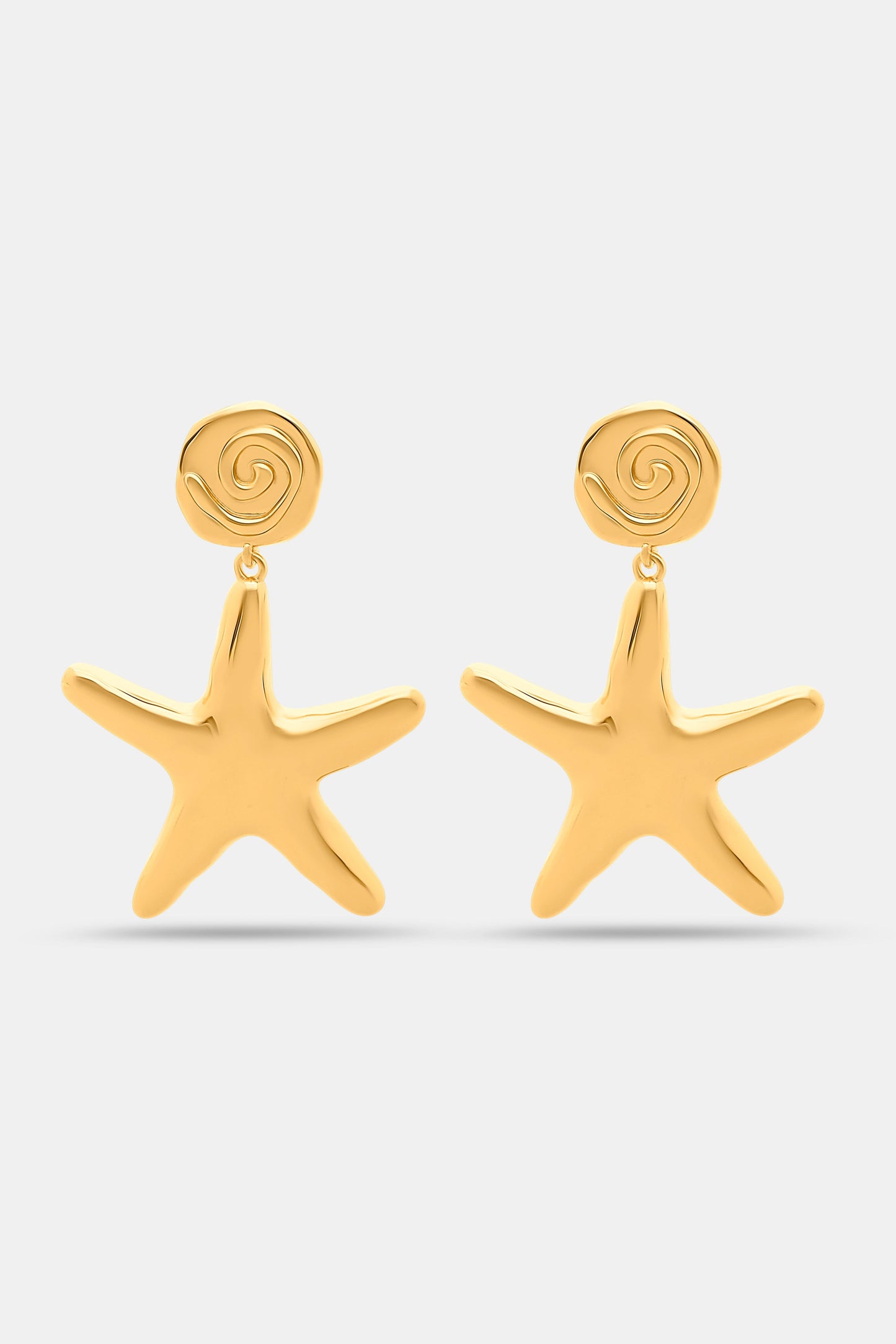 Close-up of a person’s ear with Roller Rabbit Starfish Drop Earrings—gold-tone danglers featuring a small rose detail—against curly dark hair and tan skin.