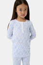 A young girl with long brown hair stands barefoot in Roller Rabbit Kids Seaside Knots Juniper Pajamas, featuring matching white and light blue knot print on soft Pima fabric with long sleeves and button details, against a plain light background.