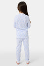 A young girl with long brown hair stands barefoot in Roller Rabbit Kids Seaside Knots Juniper Pajamas, featuring matching white and light blue knot print on soft Pima fabric with long sleeves and button details, against a plain light background.