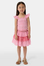 A child wears the Roller Rabbit Kids Starry Dot Sami Skirt in pink and red with star and polka dot patterns, paired with a pink smocked top, standing against a plain light background.