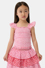 A young girl wears the Roller Rabbit Kids Starry Dot Tory Top in pastel pink with flutter sleeves, paired with a matching skirt featuring red stars and white polka dots. Only her torso and part of her face are visible.