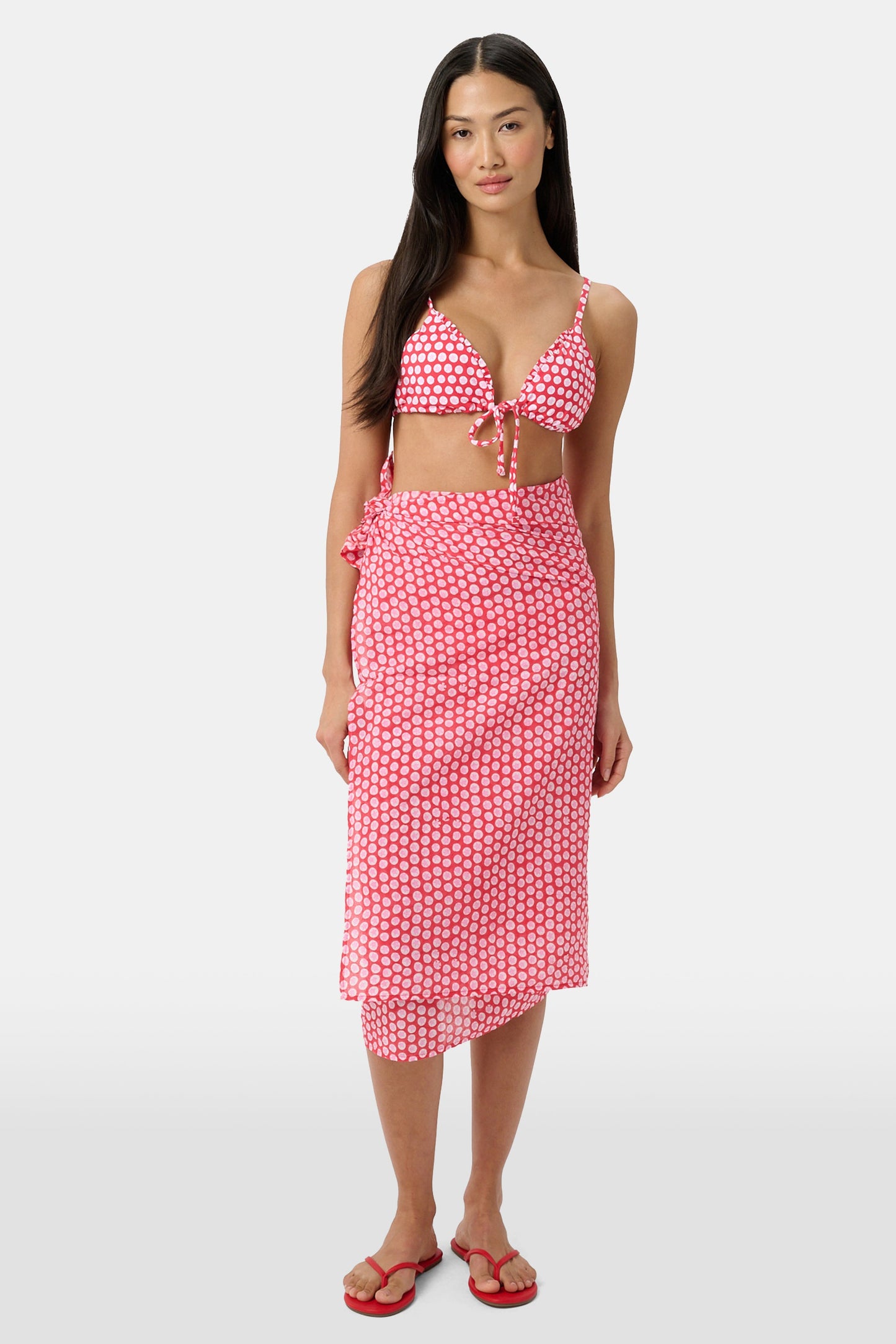 A woman models the Roller Rabbit Starry Dot Pareo with a pink and white bikini top and red flip-flops, standing against a light background.