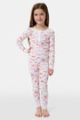A young girl smiles barefoot in Roller Rabbit Kids Summer Memories Pajamas, made from soft Pima Cotton with playful, colorful prints on white. She stands against a light gray background. Made in Peru.