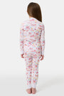 A young girl smiles barefoot in Roller Rabbit Kids Summer Memories Pajamas, made from soft Pima Cotton with playful, colorful prints on white. She stands against a light gray background. Made in Peru.