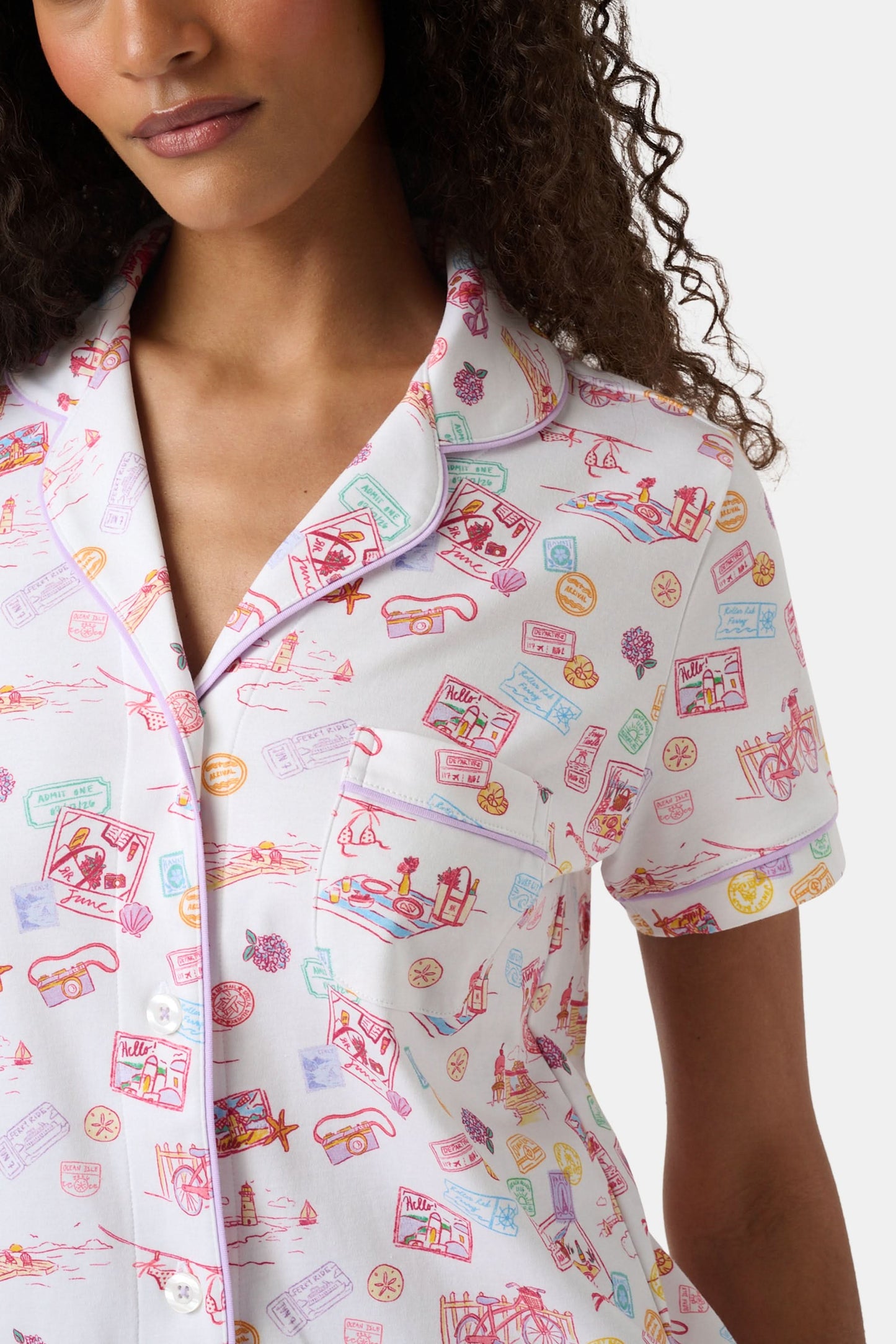 A woman with curly hair models the Roller Rabbit Summer Memories Fiora Pajamas, a Pima cotton set with a colorful sushi print, including a short-sleeve button-up top and long pants, against a white background.