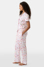 A woman with curly hair models the Roller Rabbit Summer Memories Fiora Pajamas, a Pima cotton set with a colorful sushi print, including a short-sleeve button-up top and long pants, against a white background.