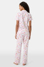 A woman with curly hair models the Roller Rabbit Summer Memories Fiora Pajamas, a Pima cotton set with a colorful sushi print, including a short-sleeve button-up top and long pants, against a white background.