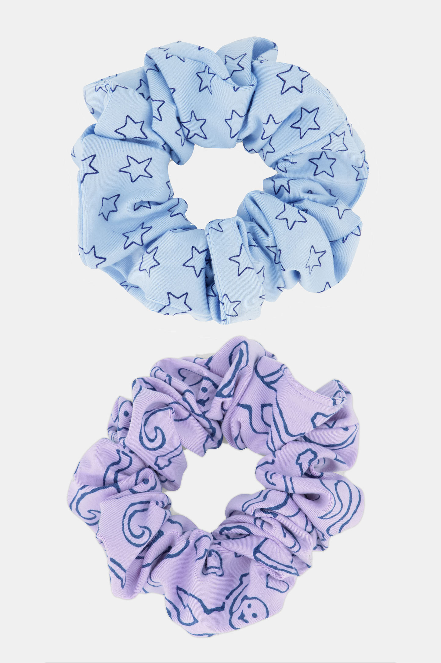 The Assorted Scrunchies Set Of 2 features a light blue scrunchie with dark blue stars and a lavender one with dark blue moons and abstract shapes—fun, stylish hair accessories for any look.