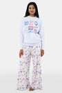 A woman with long dark hair wears the Roller Rabbit Tinned or Twist Crewneck, a light blue cotton fleece pullover with colorful sardine can and fish illustrations, paired with matching white pants featuring food-themed patterns against a plain white background.