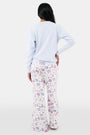 A woman with long dark hair wears the Roller Rabbit Tinned or Twist Crewneck, a light blue cotton fleece pullover with colorful sardine can and fish illustrations, paired with matching white pants featuring food-themed patterns against a plain white background.