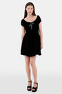 A woman faces forward in the Roller Rabbit Velvet Tilly Dress, a short-sleeve black velvet mini with a floral bow at the neckline, paired with black platform sandals, set against a plain light background.