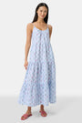 A woman with long hair stands facing forward, wearing the Roller Rabbit Wildflower Jemina Dakota Dress in sky blue and pink sandals.