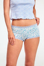 The Roller Rabbit Classic Core Boyshort 4 Pack includes four pairs of girls' underwear in fun patterns—green diamond, white with blue florals, mint with hearts, and light blue floral—all made from soft modal fabric for comfort.