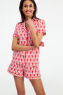 A woman smiles with folded arms, wearing Monkey Polo Pajamas—red and white short-sleeve pima cotton pajamas featuring a playful all-over monkey print—against a plain white background.