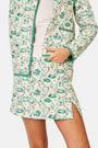 A person wears the Roller Rabbit Woodland Toile Quilted Azure Mini Skirt, featuring green floral patterns, green trim, a side slit, and paired with a matching white jacket—an ideal fall fashion ensemble.