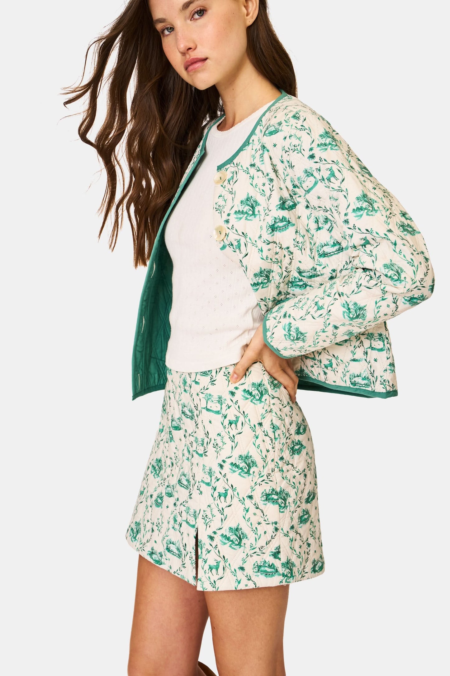 A person wears the Roller Rabbit Woodland Toile Quilted Azure Mini Skirt, featuring green floral patterns, green trim, a side slit, and paired with a matching white jacket—an ideal fall fashion ensemble.