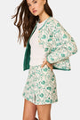 A person wears the Roller Rabbit Woodland Toile Quilted Azure Mini Skirt, featuring green floral patterns, green trim, a side slit, and paired with a matching white jacket—an ideal fall fashion ensemble.