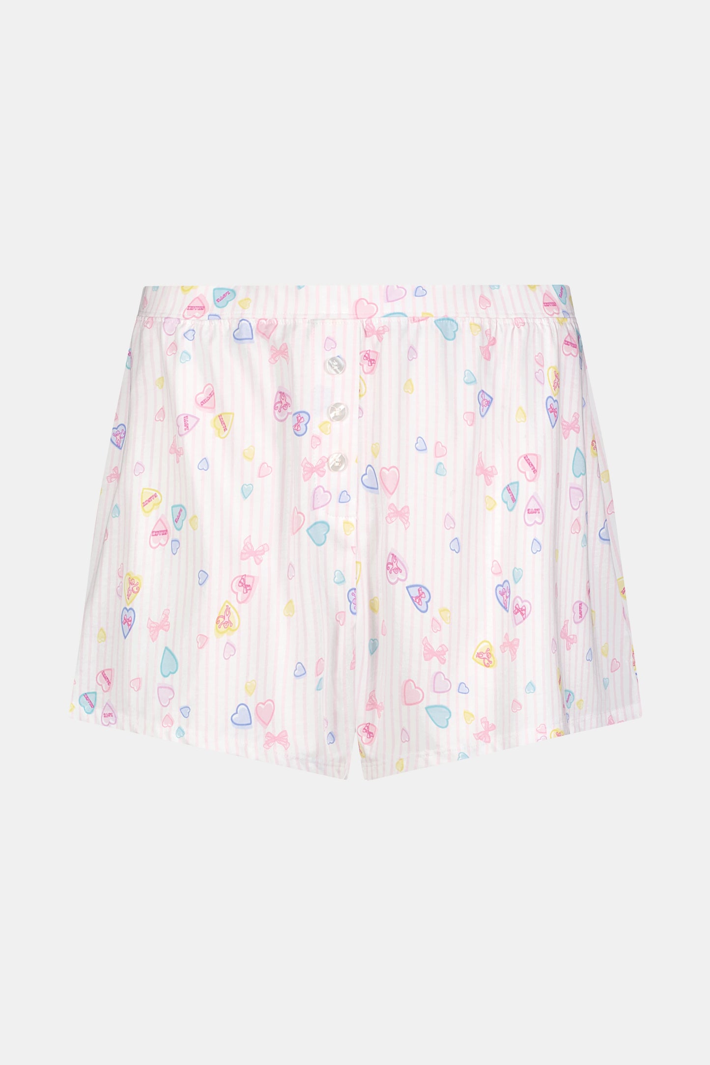 Wearing Roller Rabbit's Candy Heart Stripe Jones Shortie pajama shorts, featuring a pastel hearts, bows, and stars pattern, this person stands against a light background.