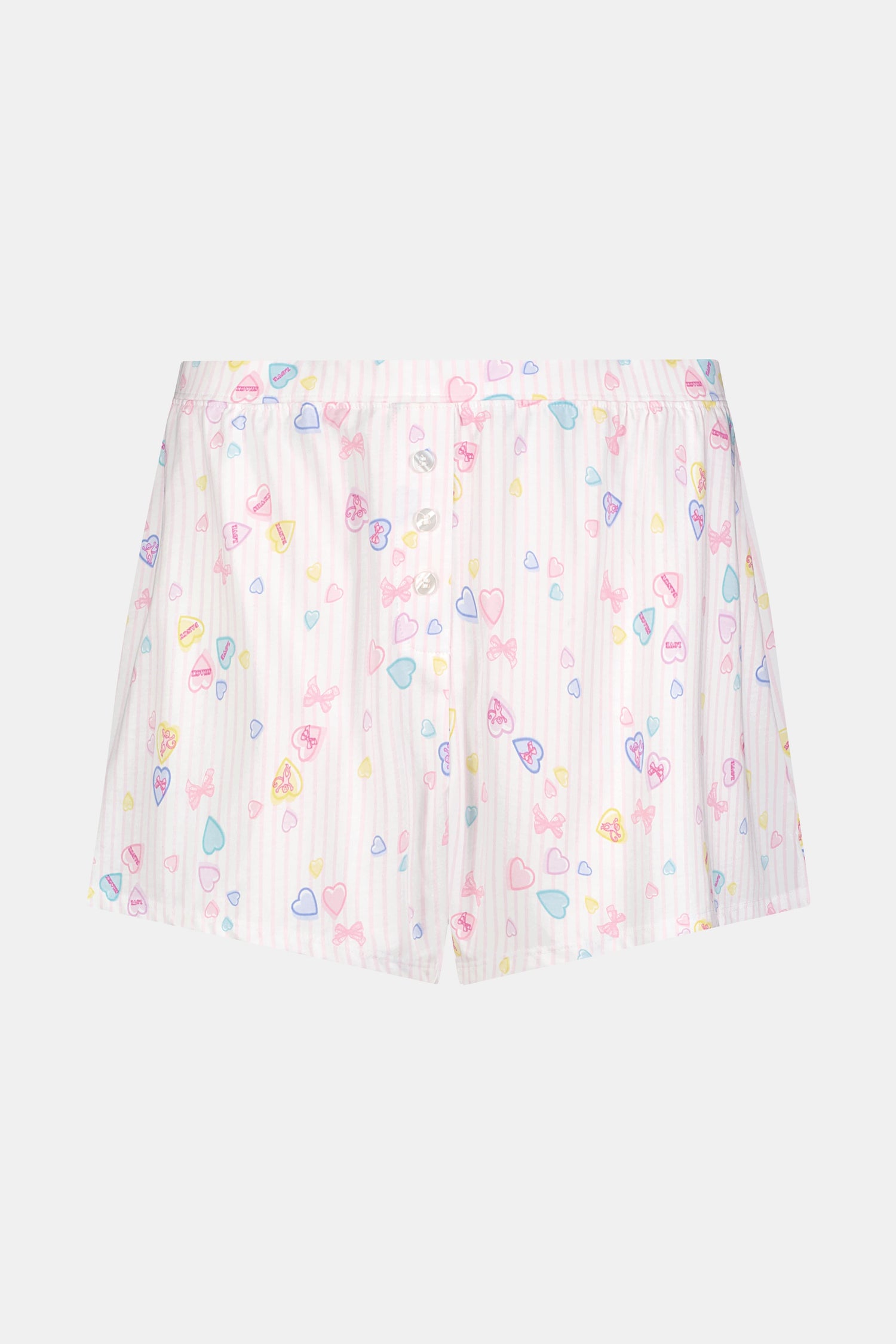Wearing Roller Rabbit's Candy Heart Stripe Jones Shortie pajama shorts, featuring a pastel hearts, bows, and stars pattern, this person stands against a light background.