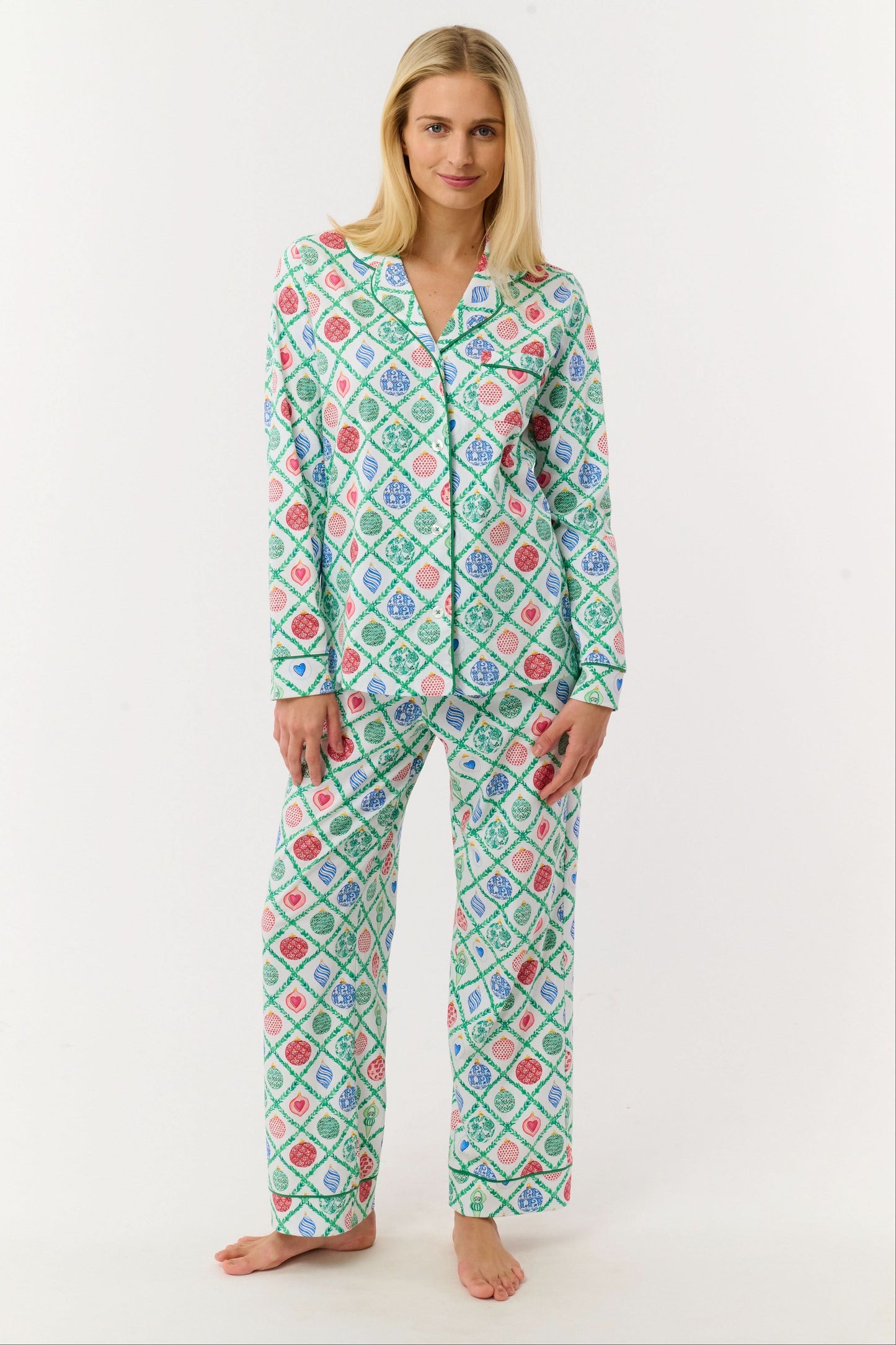 A woman stands barefoot against a white background, wearing Roller Rabbit Ornament Trellis Long Sleeve Polo Pajamas—holiday PJs with a blue, green, and pink geometric diamond print, made from 100 Pima cotton.