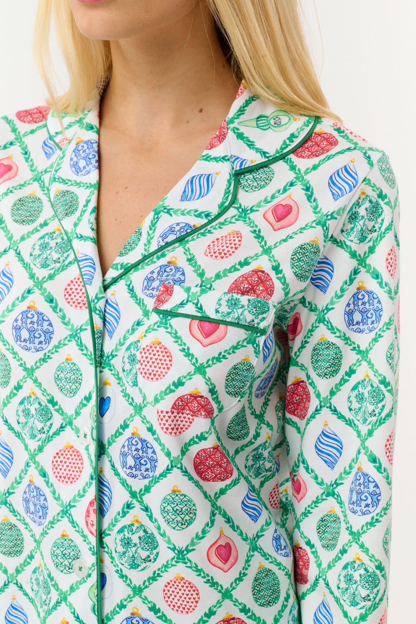 A woman stands barefoot against a white background, wearing Roller Rabbit Ornament Trellis Long Sleeve Polo Pajamas—holiday PJs with a blue, green, and pink geometric diamond print, made from 100 Pima cotton.