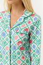 A woman stands barefoot against a white background, wearing Roller Rabbit Ornament Trellis Long Sleeve Polo Pajamas—holiday PJs with a blue, green, and pink geometric diamond print, made from 100 Pima cotton.