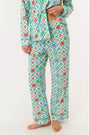 A woman stands barefoot against a white background, wearing Roller Rabbit Ornament Trellis Long Sleeve Polo Pajamas—holiday PJs with a blue, green, and pink geometric diamond print, made from 100 Pima cotton.