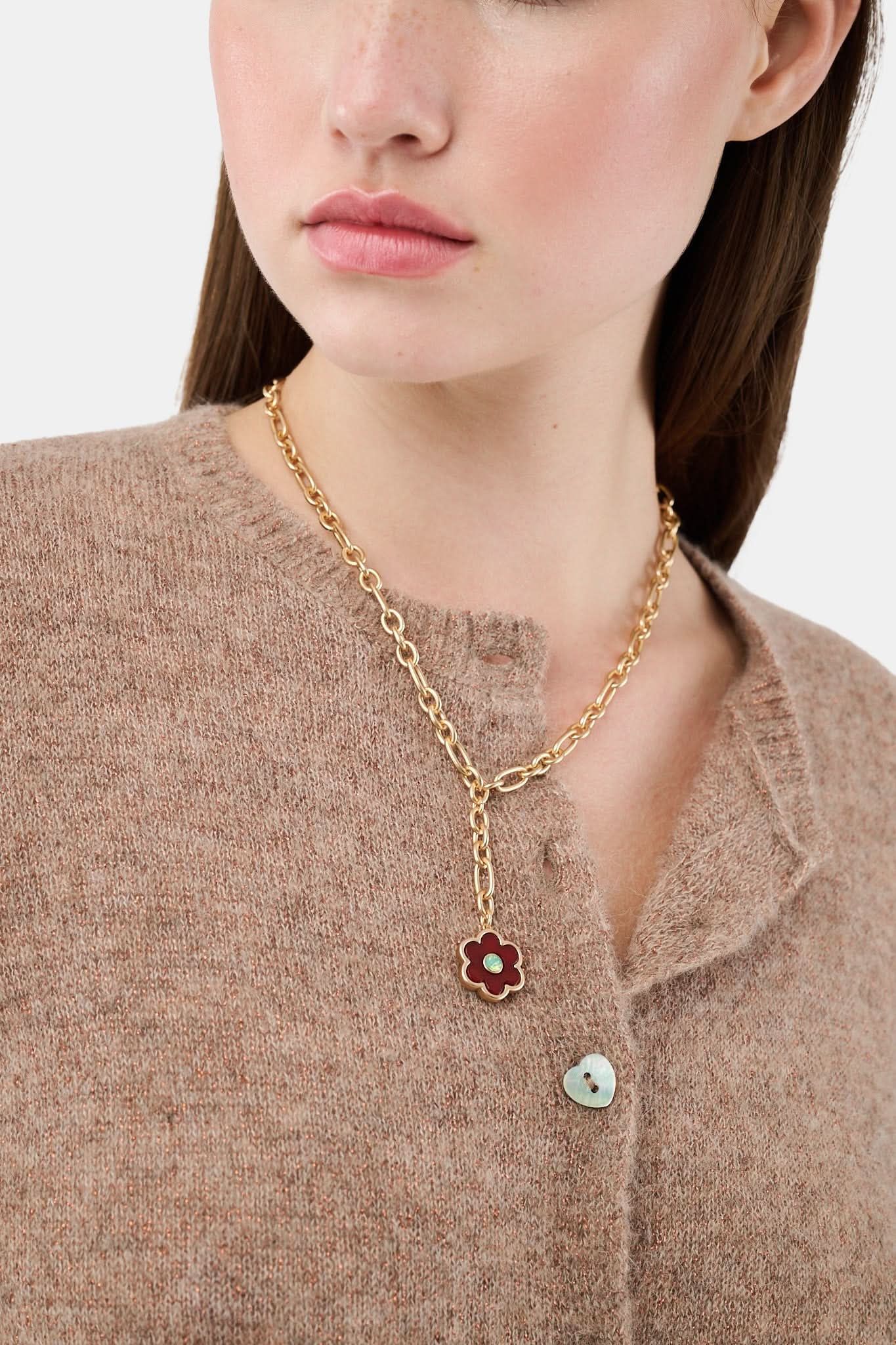 The Raya Floral Necklace by Roller Rabbit features a burgundy floral pendant with a green center on a gold chain, displayed against a white background.
