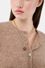 The Raya Floral Necklace by Roller Rabbit features a burgundy floral pendant with a green center on a gold chain, displayed against a white background.